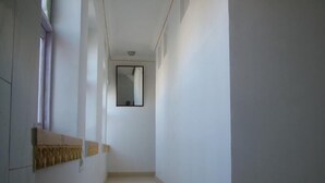 A narrow hallway with a tiled floor, a window with curtains, and a mirror on the wall. - Bhanwar Vilas Guest House (Udaipur)