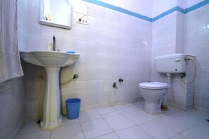 Un baño pequeño con lavamanos pedestal, inodoro y un cubo azul.