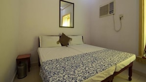 A bedroom with a bed, a bedside table, a trash can, a mirror, and a wall-mounted heater. - Bhanwar Vilas Guest House (Udaipur)