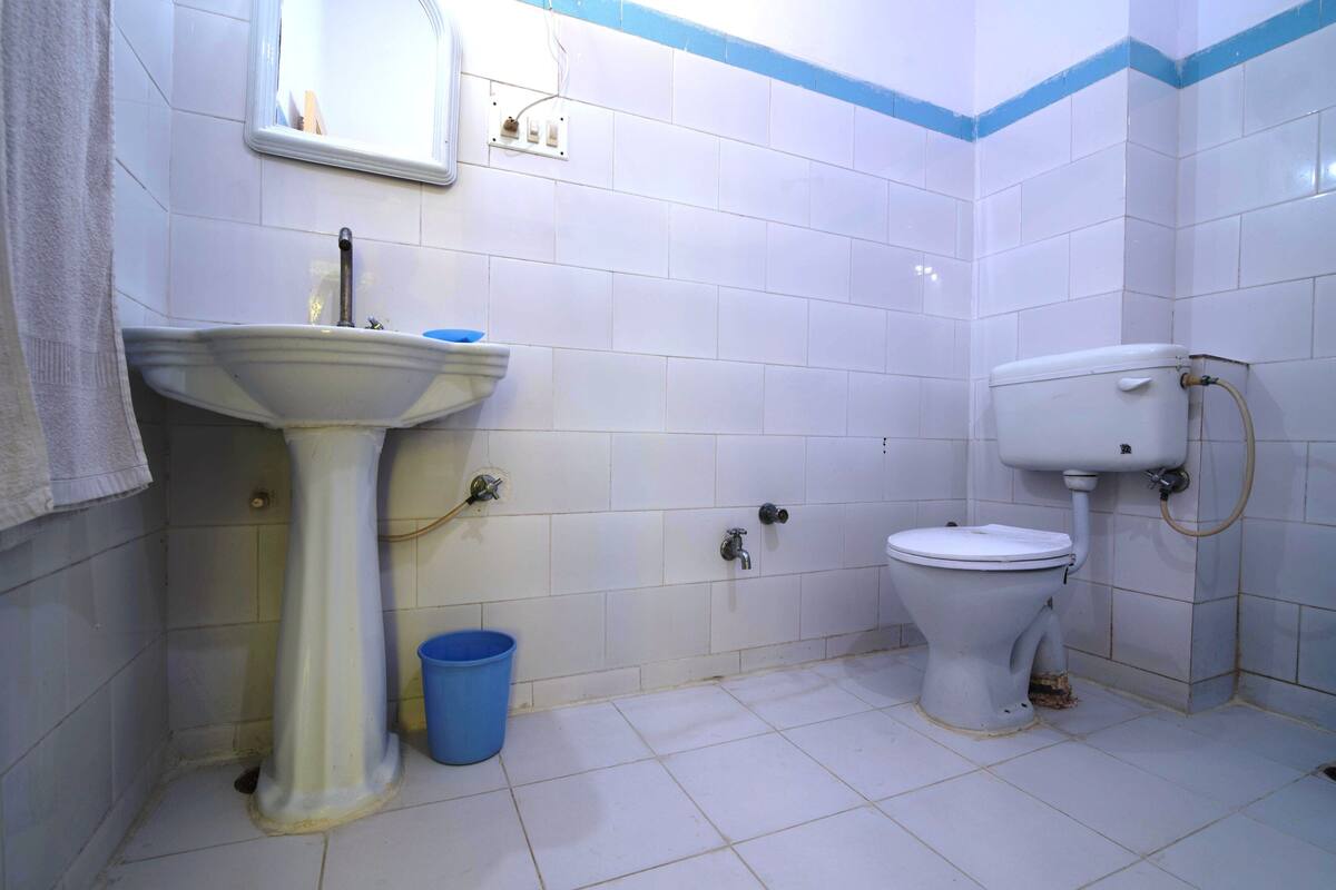 A bathroom with a pedestal sink, a toilet, and a blue bucket.