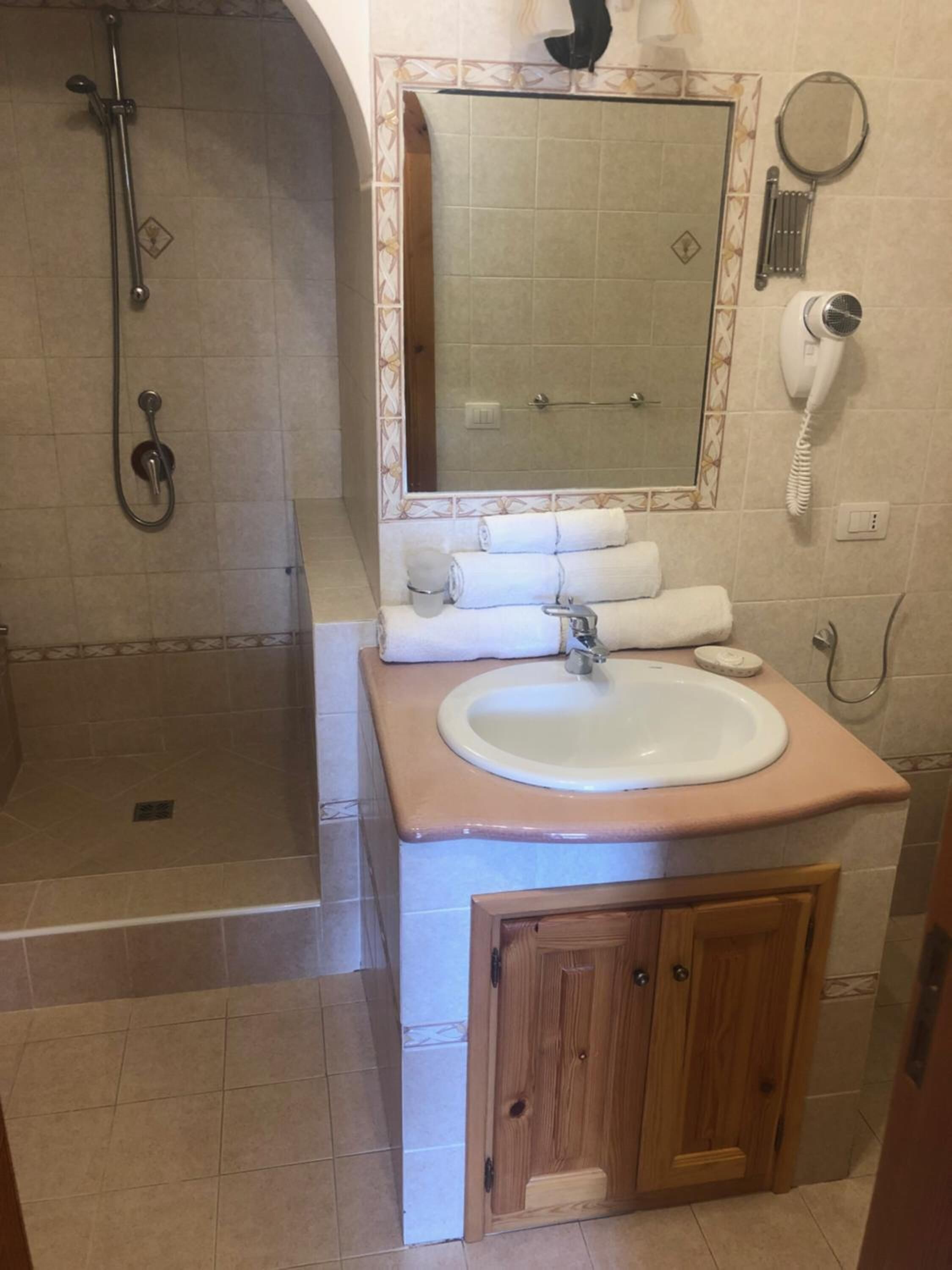 Un bagno con doccia, lavandino, specchio e asciugacapelli.
