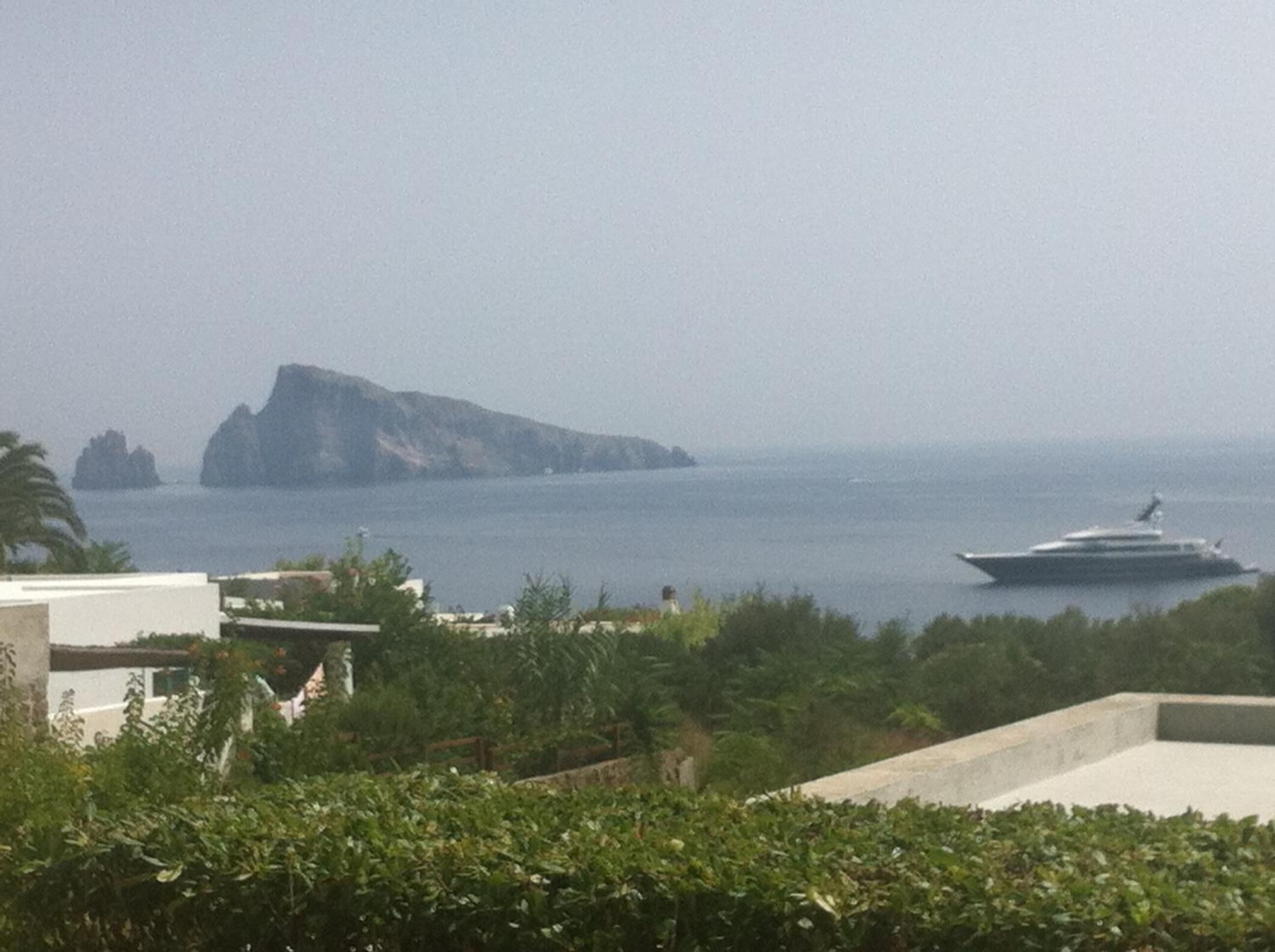 A coastal view with a yacht in the water, a prominent rock formation, and buildings in the foreground.
