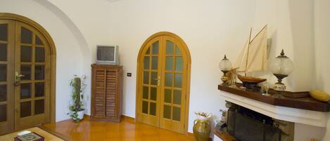 A room with a fireplace, wooden doors, a television, and a dining table.