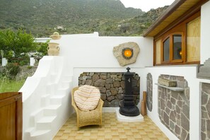 A stone fireplace with a black pillar, a wicker chair with a striped cushion, and a white wall with a wooden window frame.