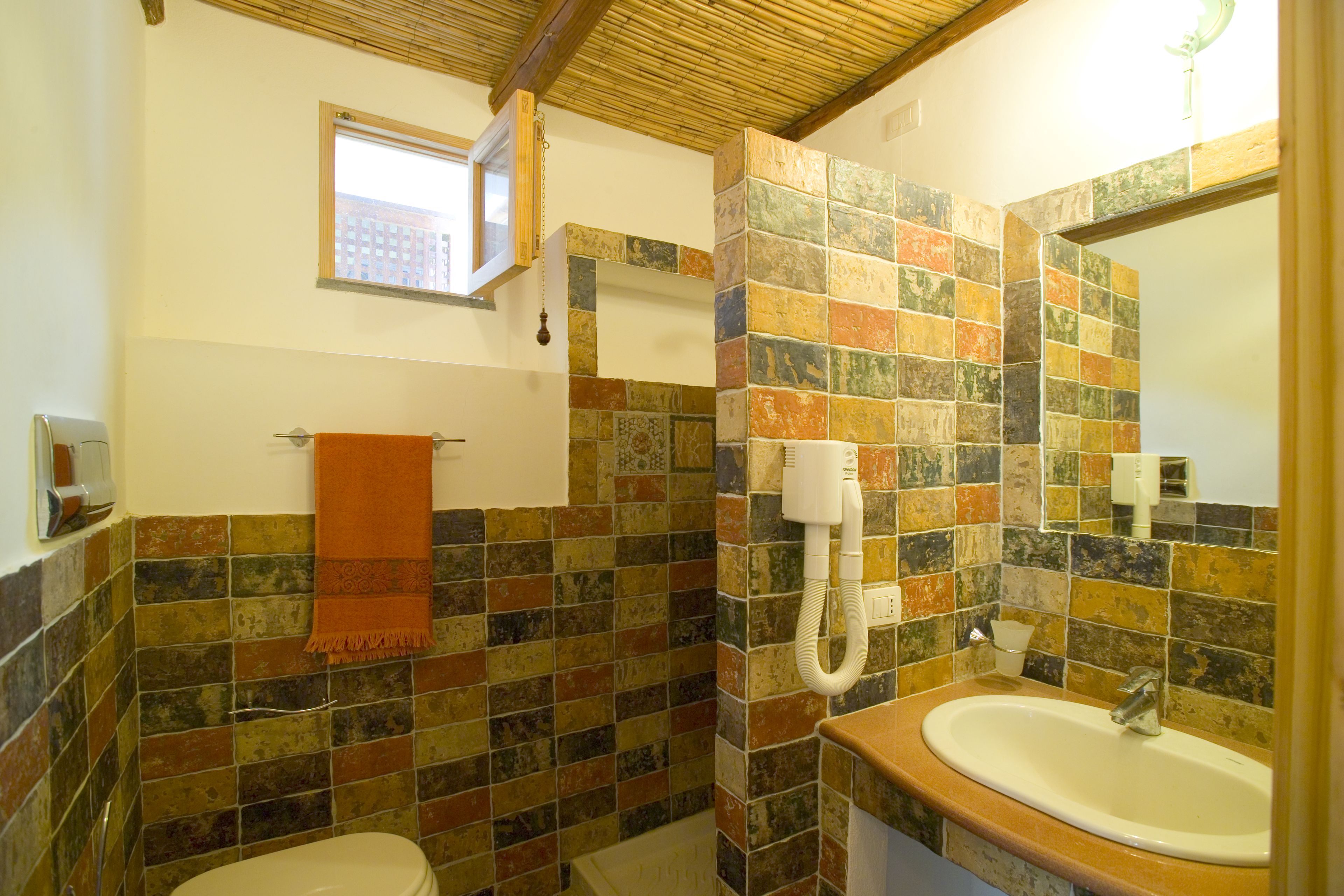 A bathroom with a tiled wall, a sink, a toilet, and a window.