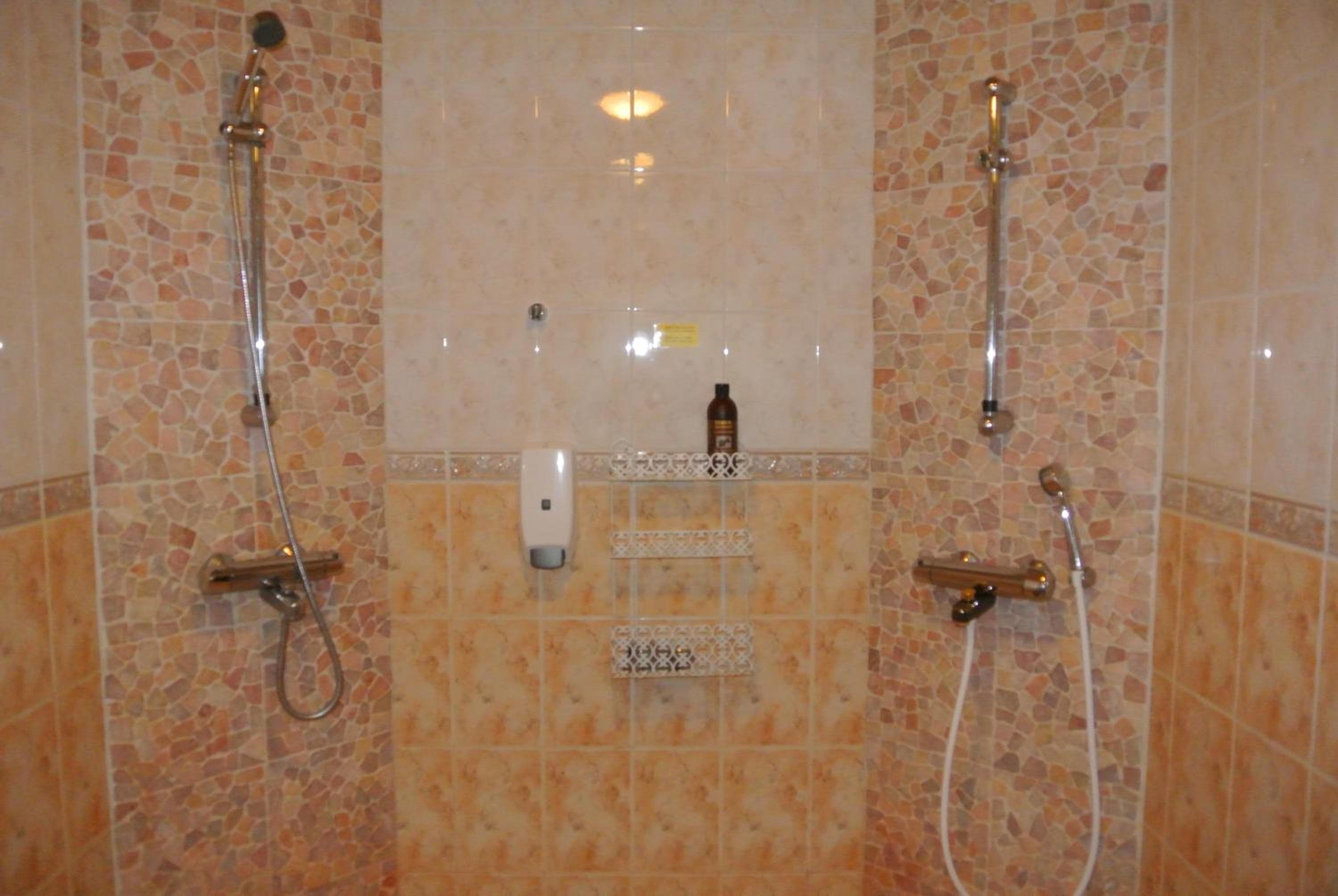 Casa de banho com paredes em mosaico, dois chuveiros e um dispensador de sabonete.