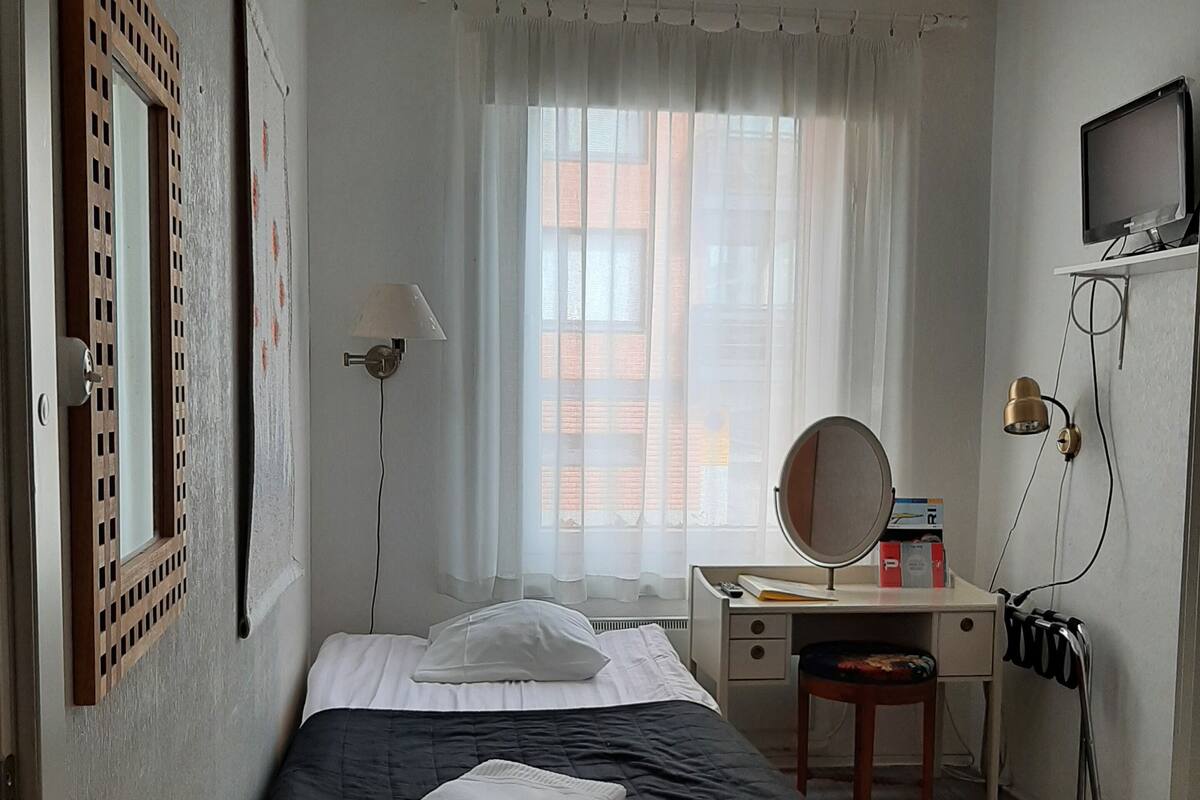 A bedroom with a bed, a desk, a chair, a television, and a window with curtains.