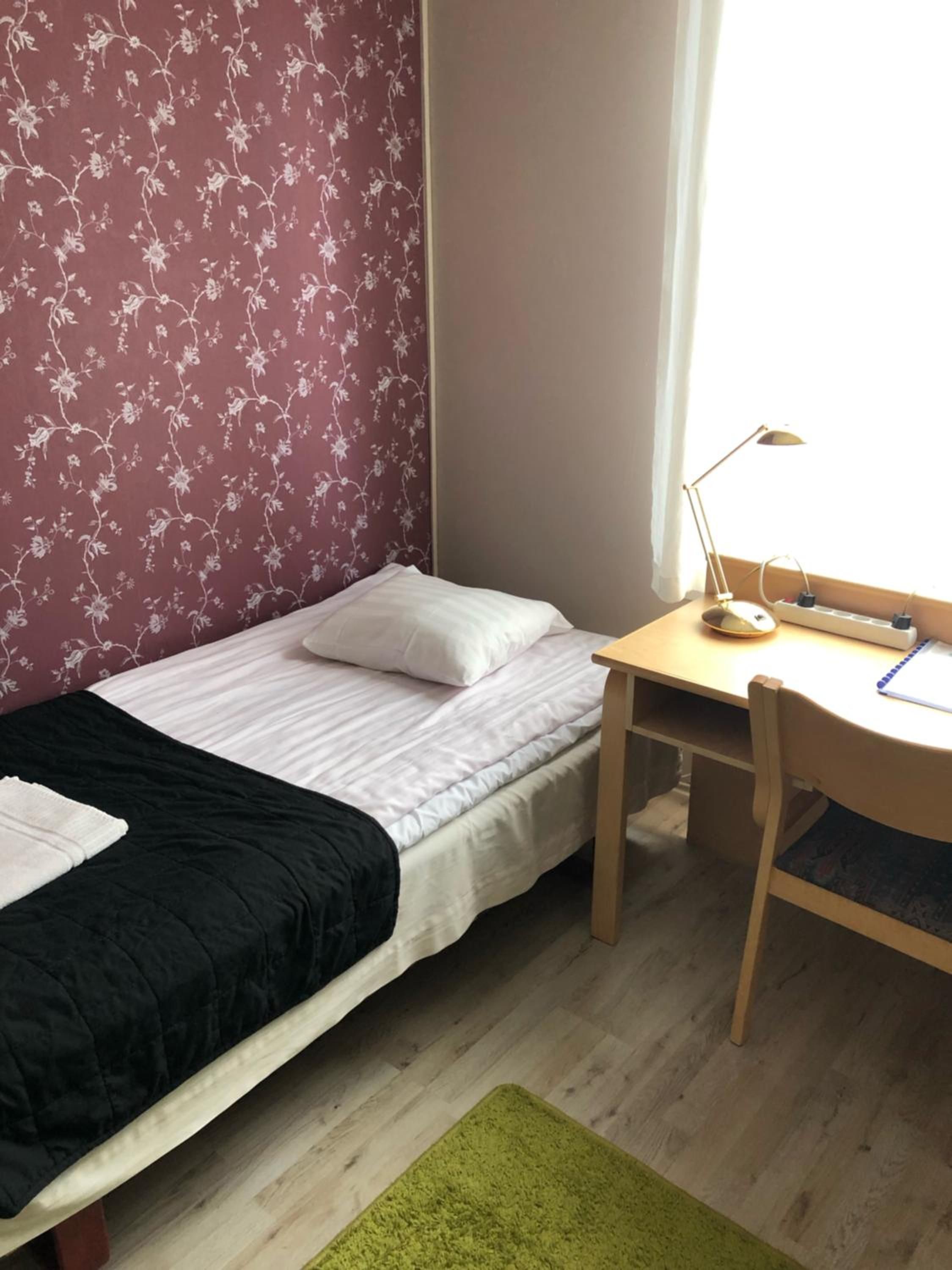 A single bed with a black and white duvet, a desk with a lamp, and a green rug.