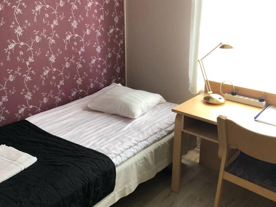 A single bed with a black and white duvet, a desk with a lamp, and a green rug.