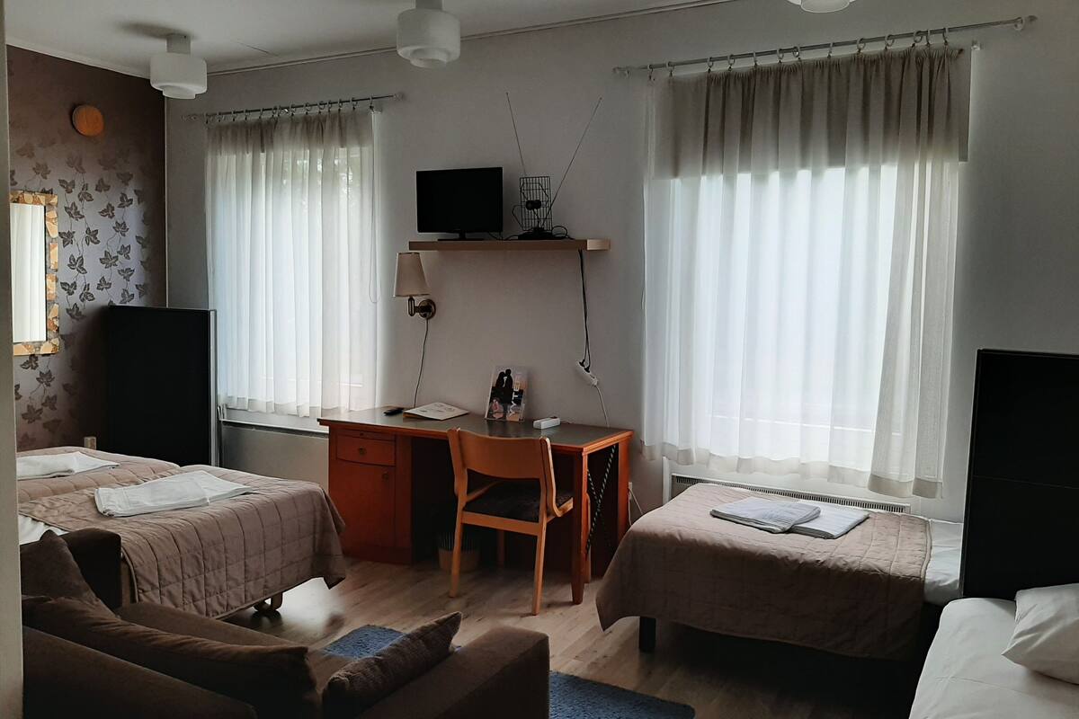 A hotel room with two beds, a desk, a chair, a TV, and a window with curtains.