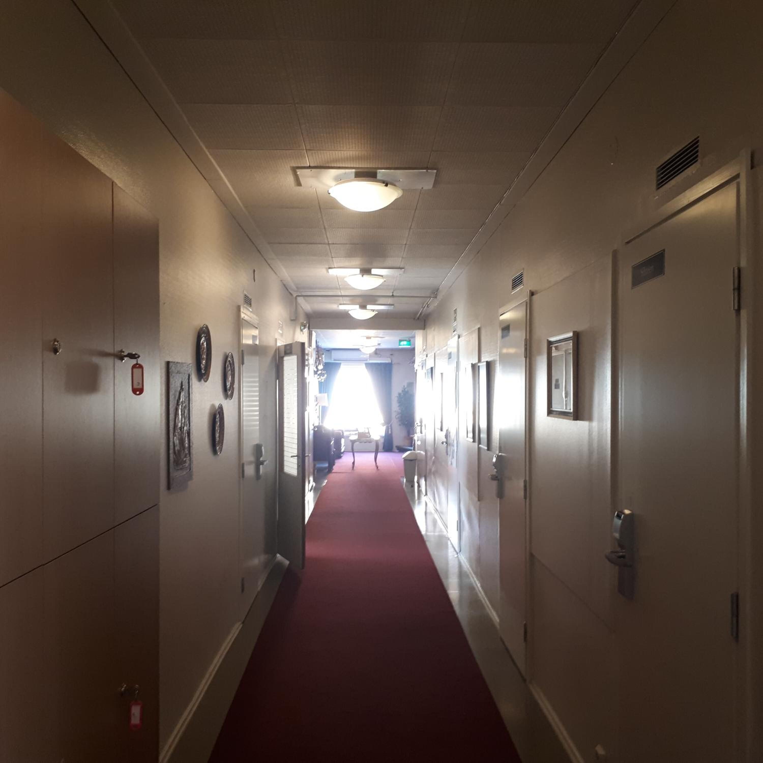 A hotel hallway with a red carpet, doors on both sides, and a ceiling with recessed lighting.