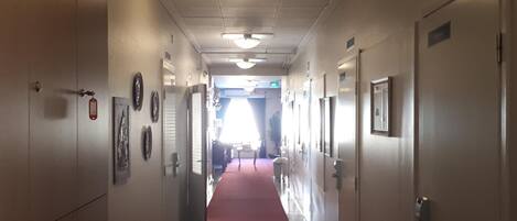 A hotel hallway with a red carpet, doors on both sides, and a ceiling with recessed lighting.
