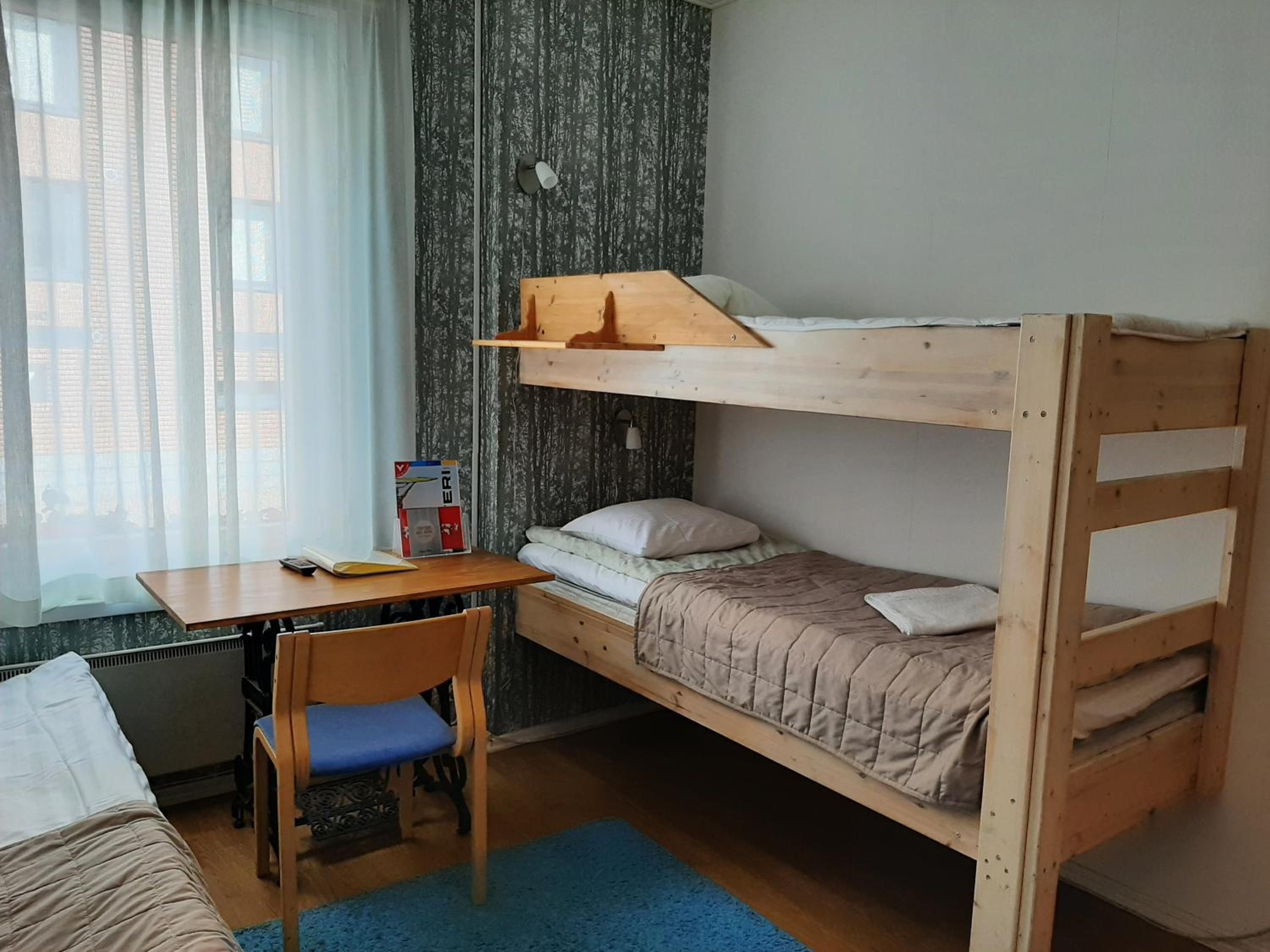 A bunk bed room with a desk and chair, a window with curtains, and a radiator.