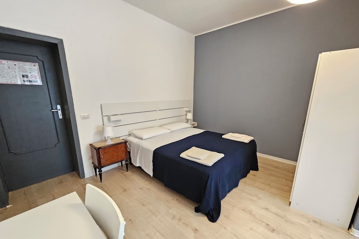 Une petite pièce propre, avec un lit, deux tables de chevet, une chaise et une porte.
