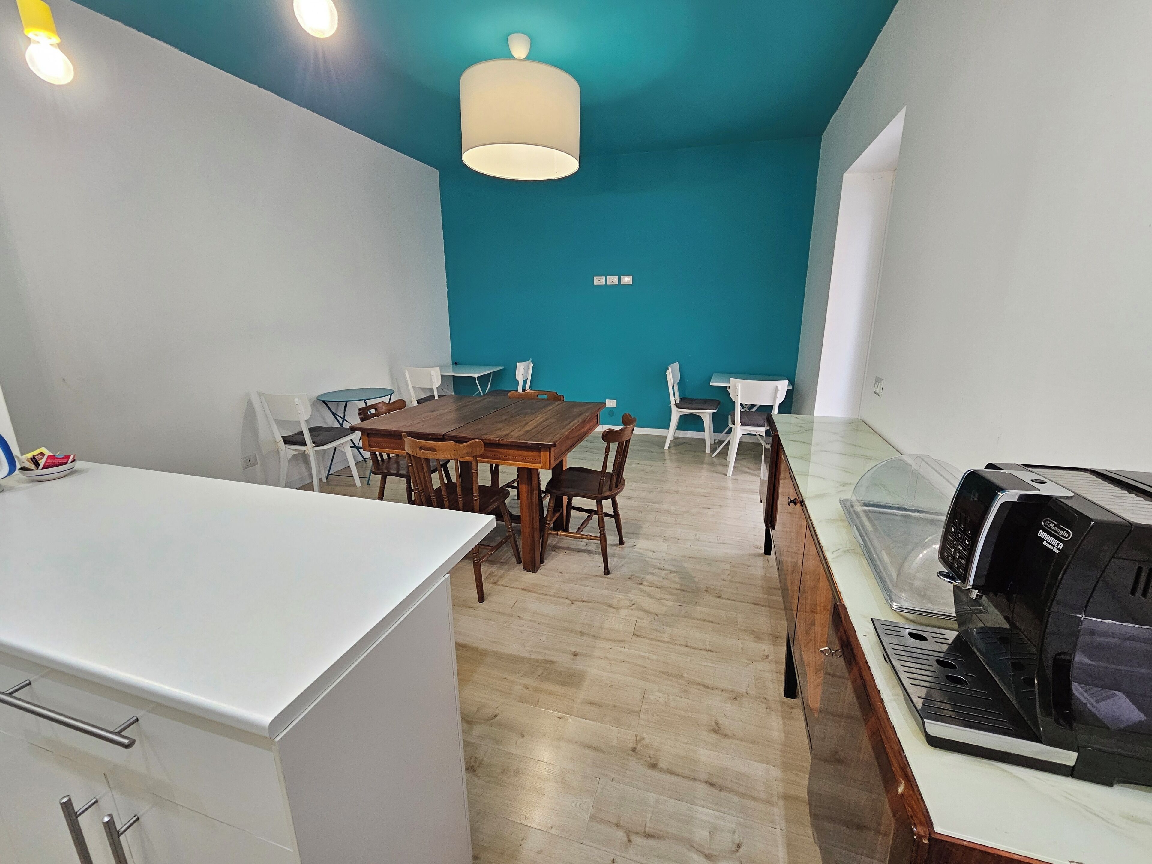 Une cuisine moderne équipée d’une machine à café, d’un coin repas avec une table et des chaises en bois, et d’un mur d’accent de couleur turquoise.