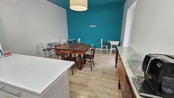 Une cuisine moderne équipée d’une machine à café, d’un coin repas avec une table et des chaises en bois, et d’un mur d’accent de couleur turquoise.