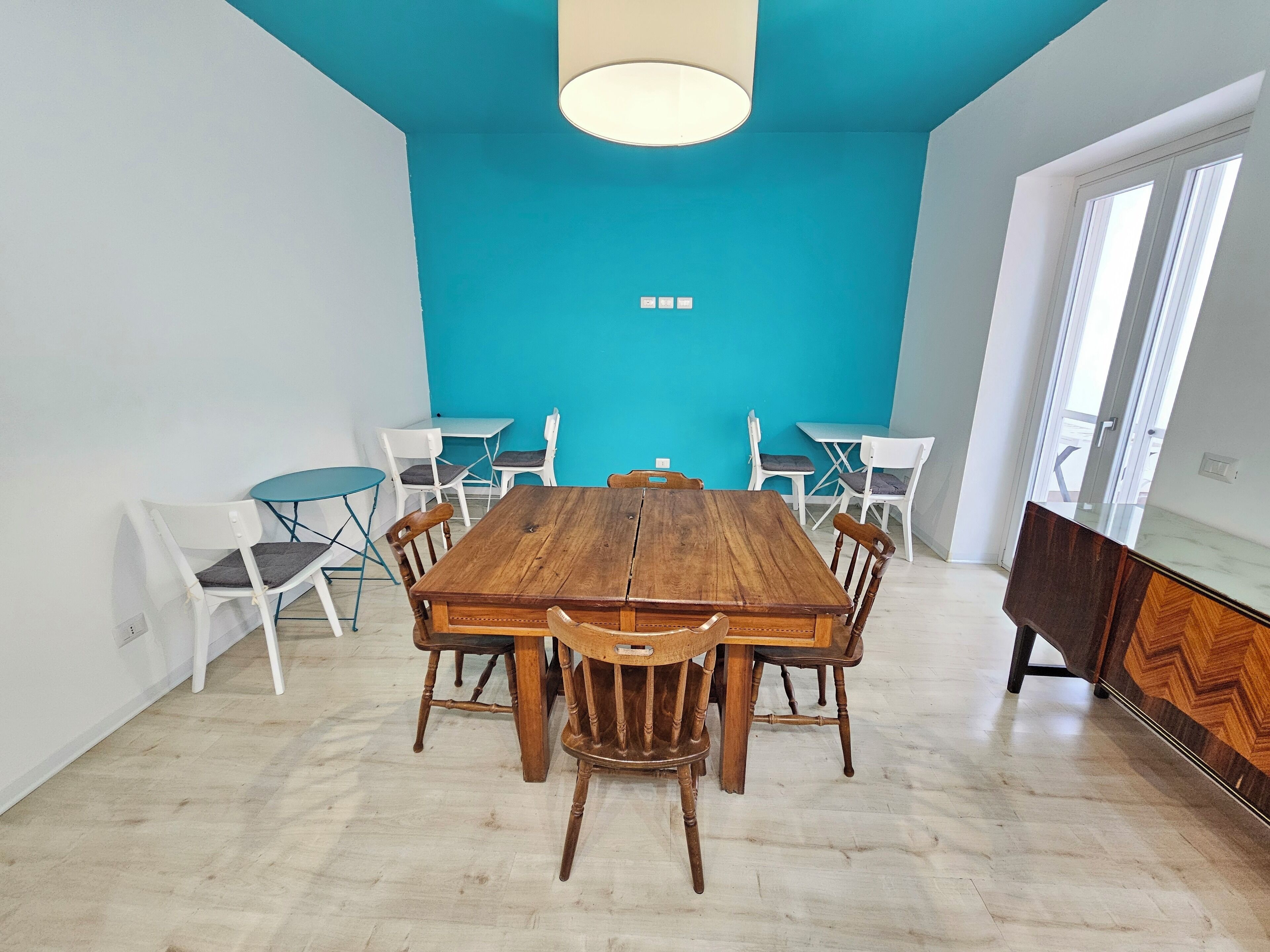 Un comedor con una mesa y sillas de madera, una pared de acento color turquesa y un amplio ventanal.