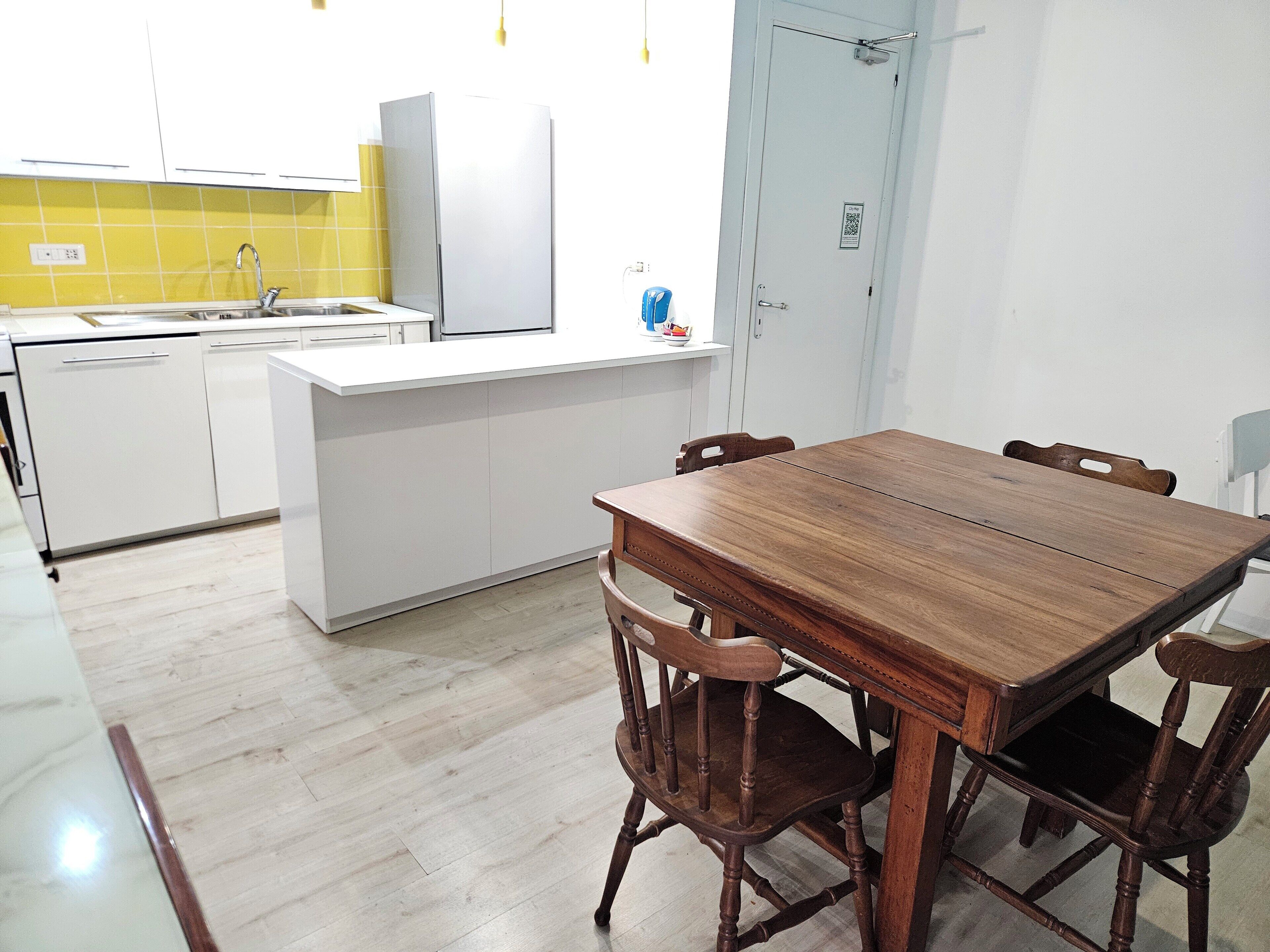 A modern kitchen with white cabinets, a wooden dining table, and a yellow backsplash.