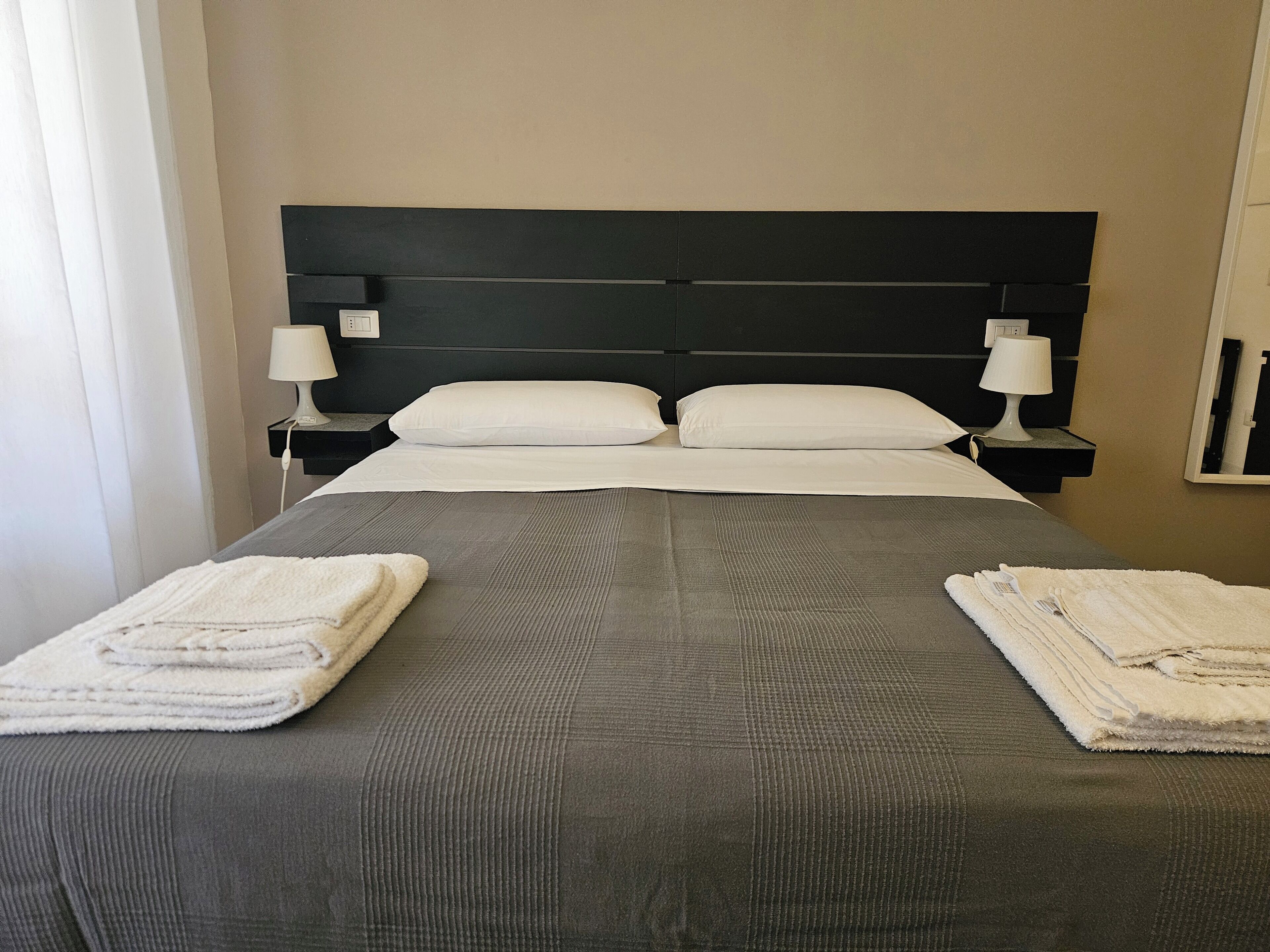 Una cama bien hecha con un cabecero oscuro, dos almohadas blancas y dos lámparas de noche.