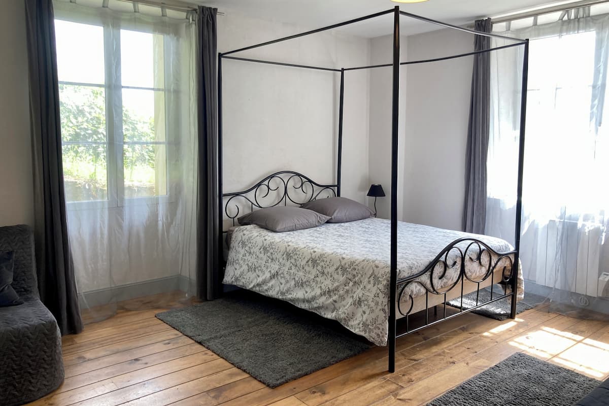 A four-poster bed with a floral bedspread, a grey rug, and a lamp on a wooden floor.