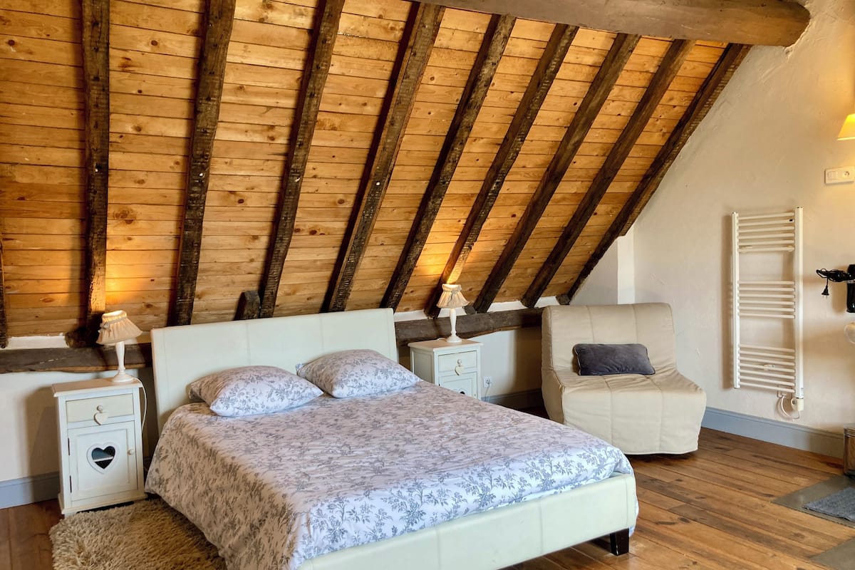 A bedroom with a sloped ceiling, a bed with floral bedding, bedside tables with lamps, and a nightstand with a heart-shaped drawer.