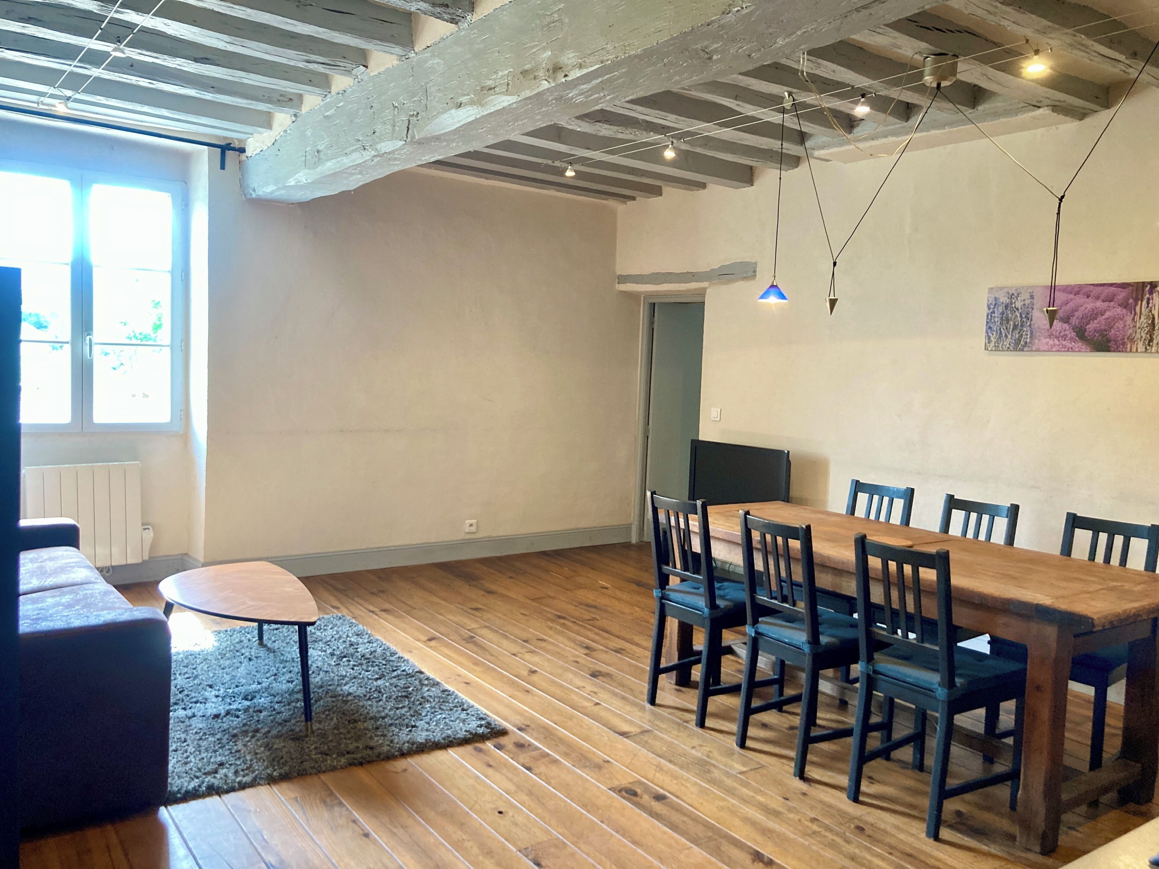 Un comedor con mesa y sillas de madera, un tapete y vigas a la vista.