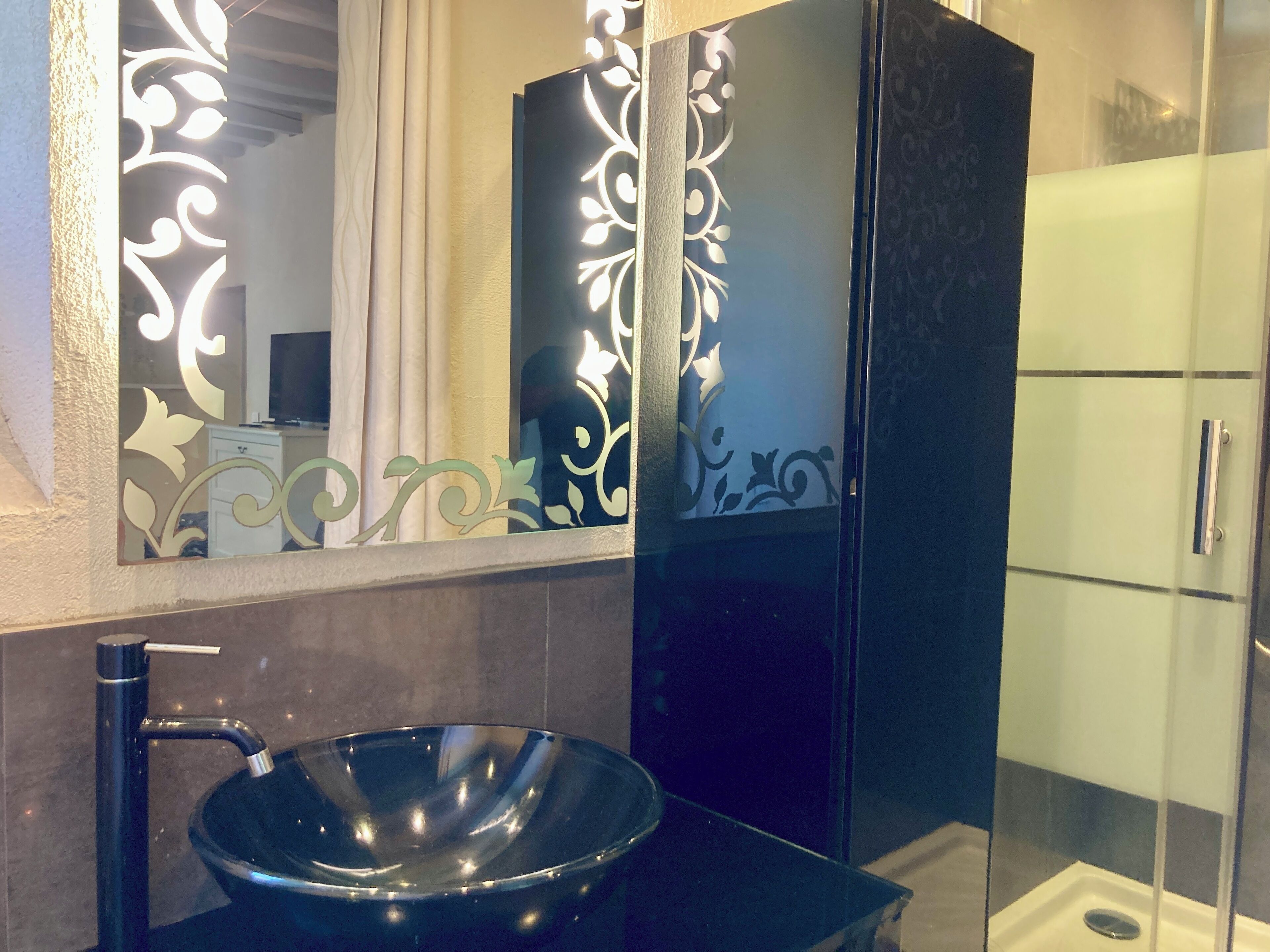 Une salle de bain moderne avec un lavabo sur pied noir, un miroir orné de motifs décoratifs et une douche à parois de verre.