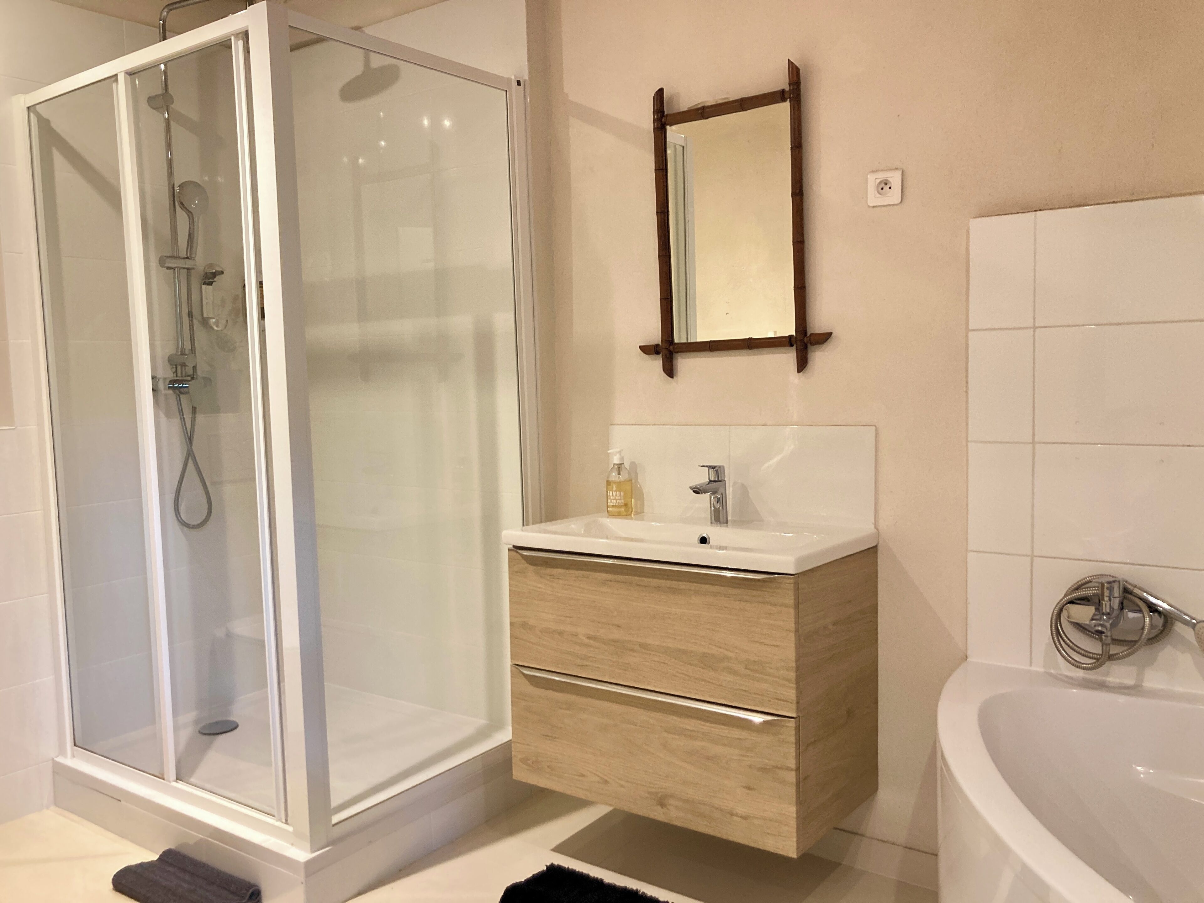 Un baño moderno con ducha de vidrio, tocador de madera con espejo y una bañera independiente.