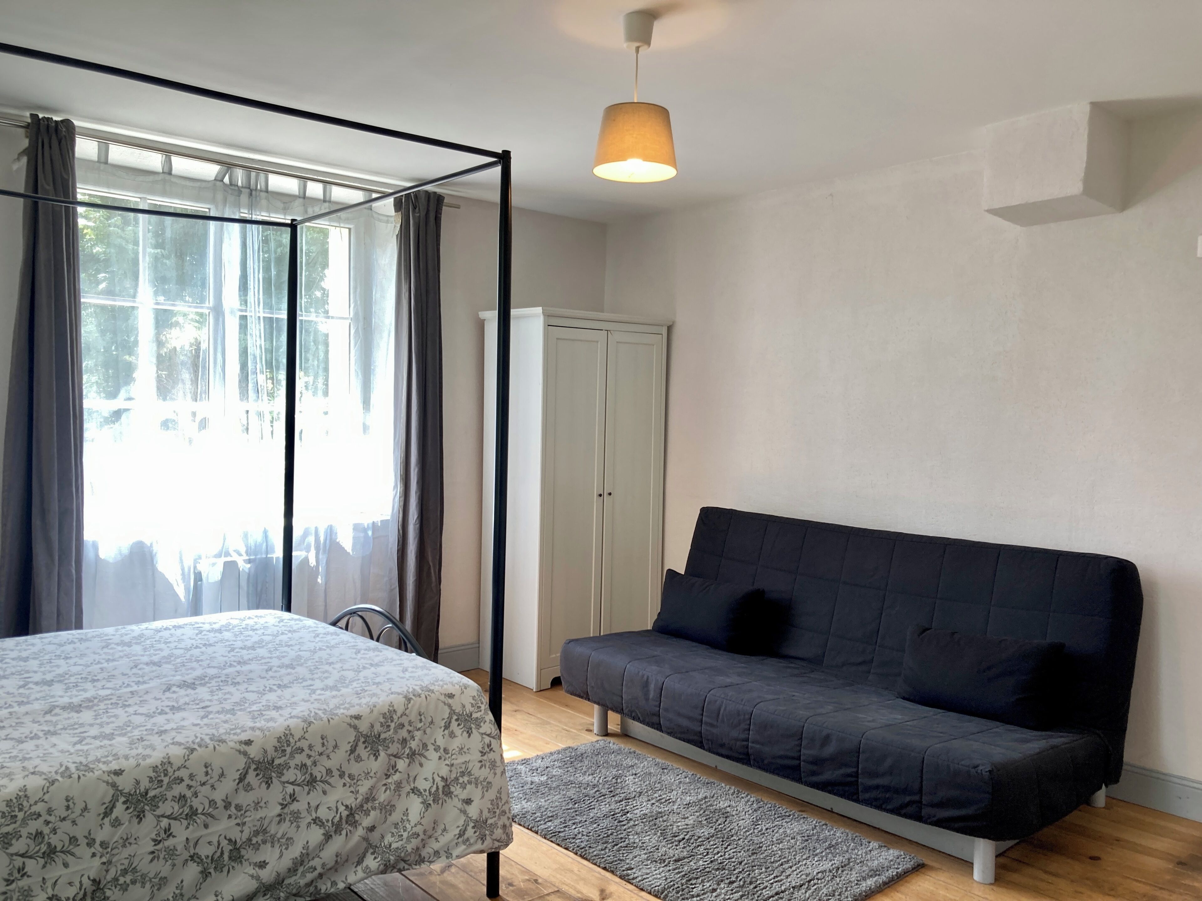 Een slaapkamer met een bed, een bank, een kledingkast en een raam met gordijnen.