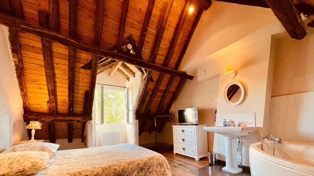 A bedroom with a large bed, a dresser, a TV, and a bathroom with a bathtub and sink. - Domaine du Moulin de Champie – Plaine de Versailles (Davron)