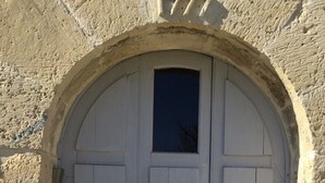 A white arched door with a small window above it, set in a textured stone wall. - Domaine du Moulin de Champie – Plaine de Versailles (Davron)