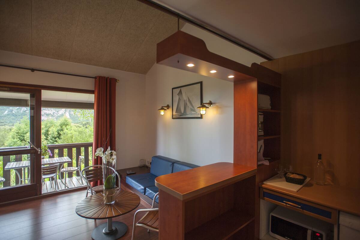 A room with a balcony, a dining area, a sofa, and a kitchen area.