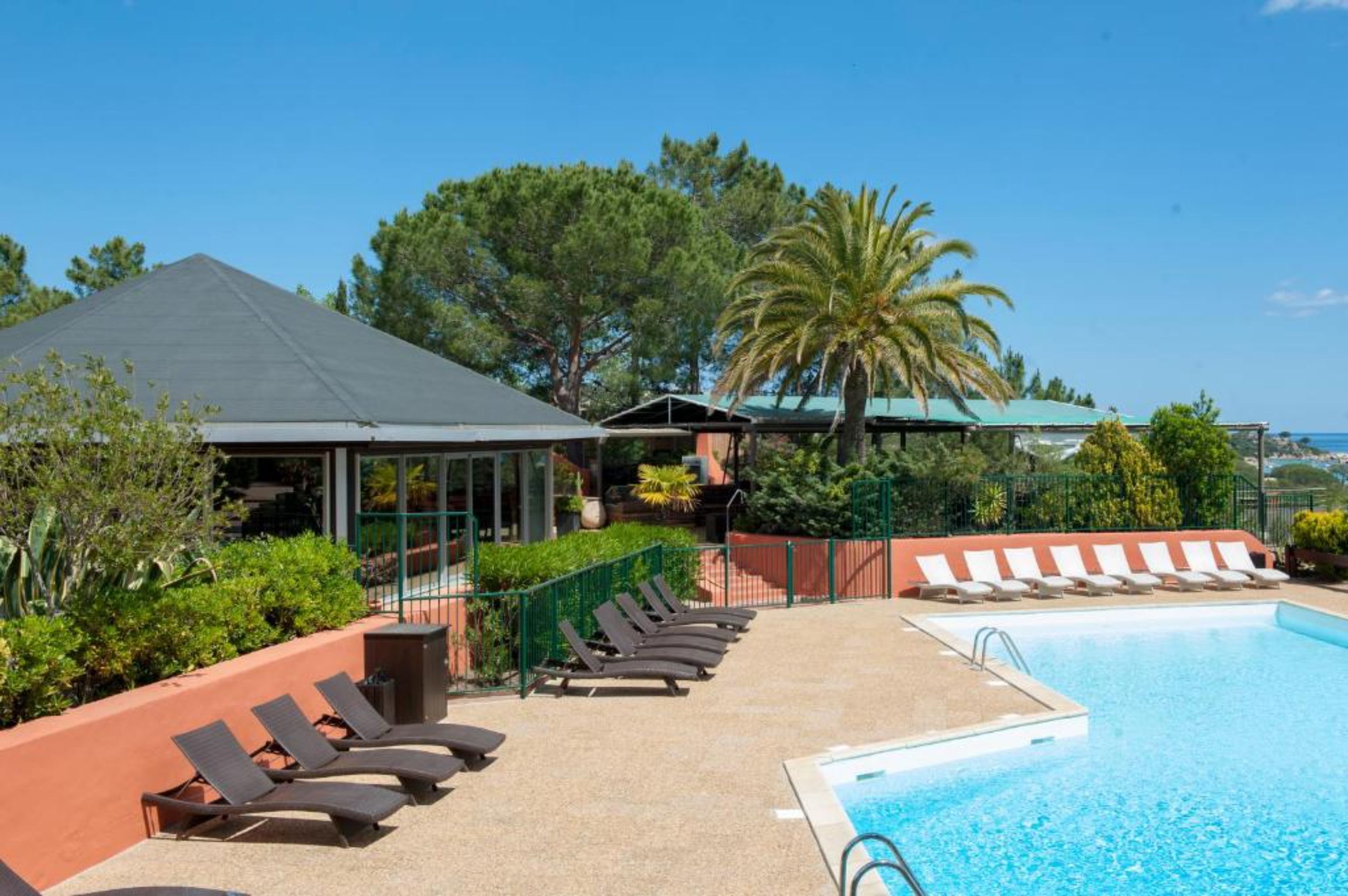 Un espace piscine avec des chaises longues, un coin salon abrité et une vue sur la mer.