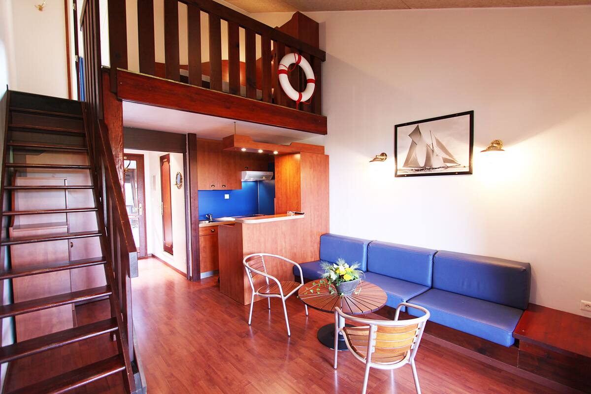 A modern interior with a wooden staircase, a blue sofa, a dining table with chairs, and a kitchen area.