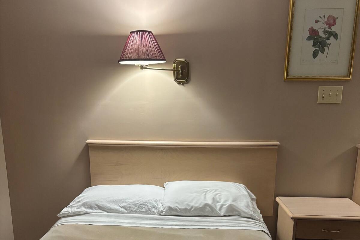 A neatly made bed with white linens, a bedside table with a lamp, and a framed picture on the wall.