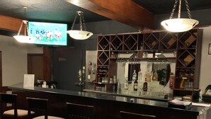 Un espace bar avec des tabourets de bar en bois, un comptoir où est affiché le menu et un téléviseur diffusant un événement sportif.