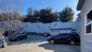 Un espace de stationnement où sont garées deux voitures devant un immeuble doté de nombreuses fenêtres et d’un garage.