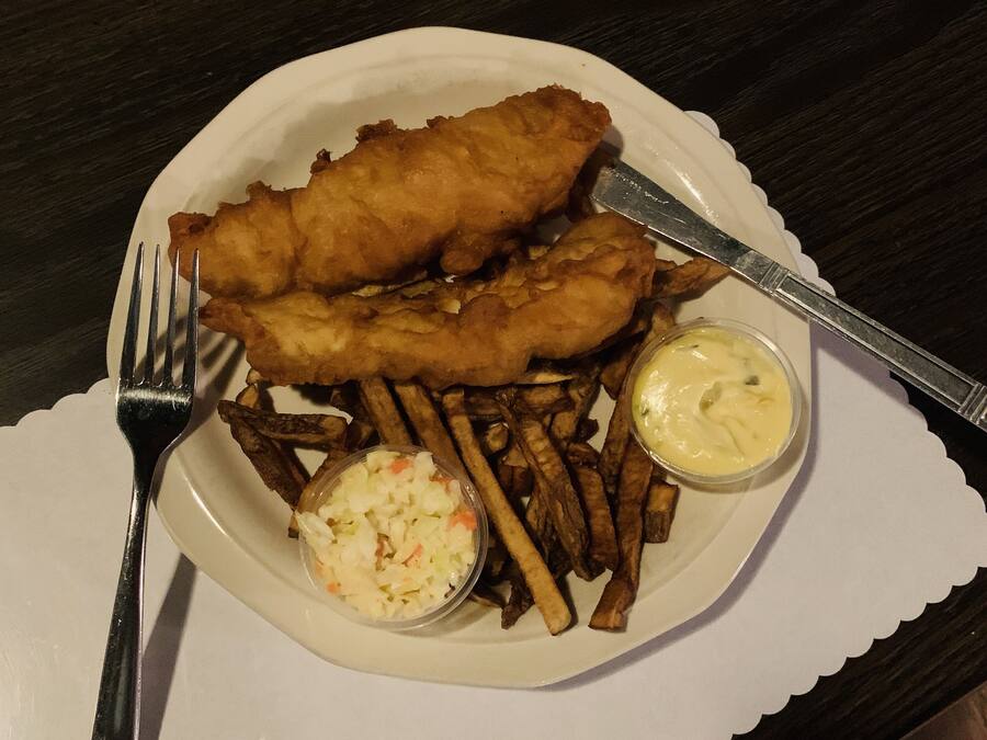 Um prato de peixe com batatas fritas, acompanhado de salada de repolho e molho tártaro.