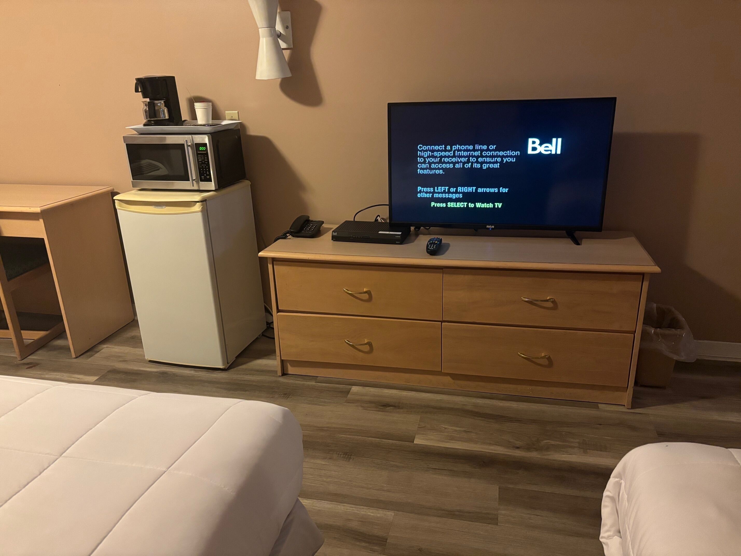 A hotel room with a bed, a desk with a computer, a television, a microwave, and a small refrigerator.