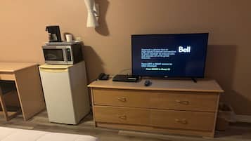 A hotel room with a bed, a desk with a computer, a television, a microwave, and a small refrigerator.