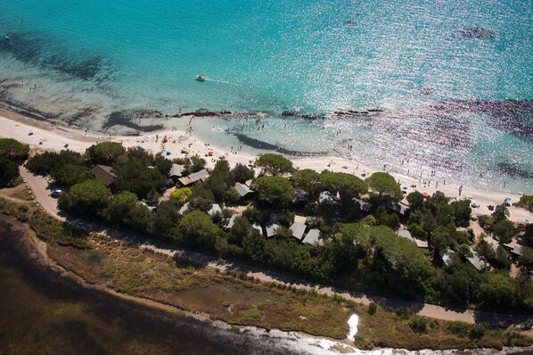 Une vue aérienne d’une zone côtière avec une plage, une route et une rangée de maisons.