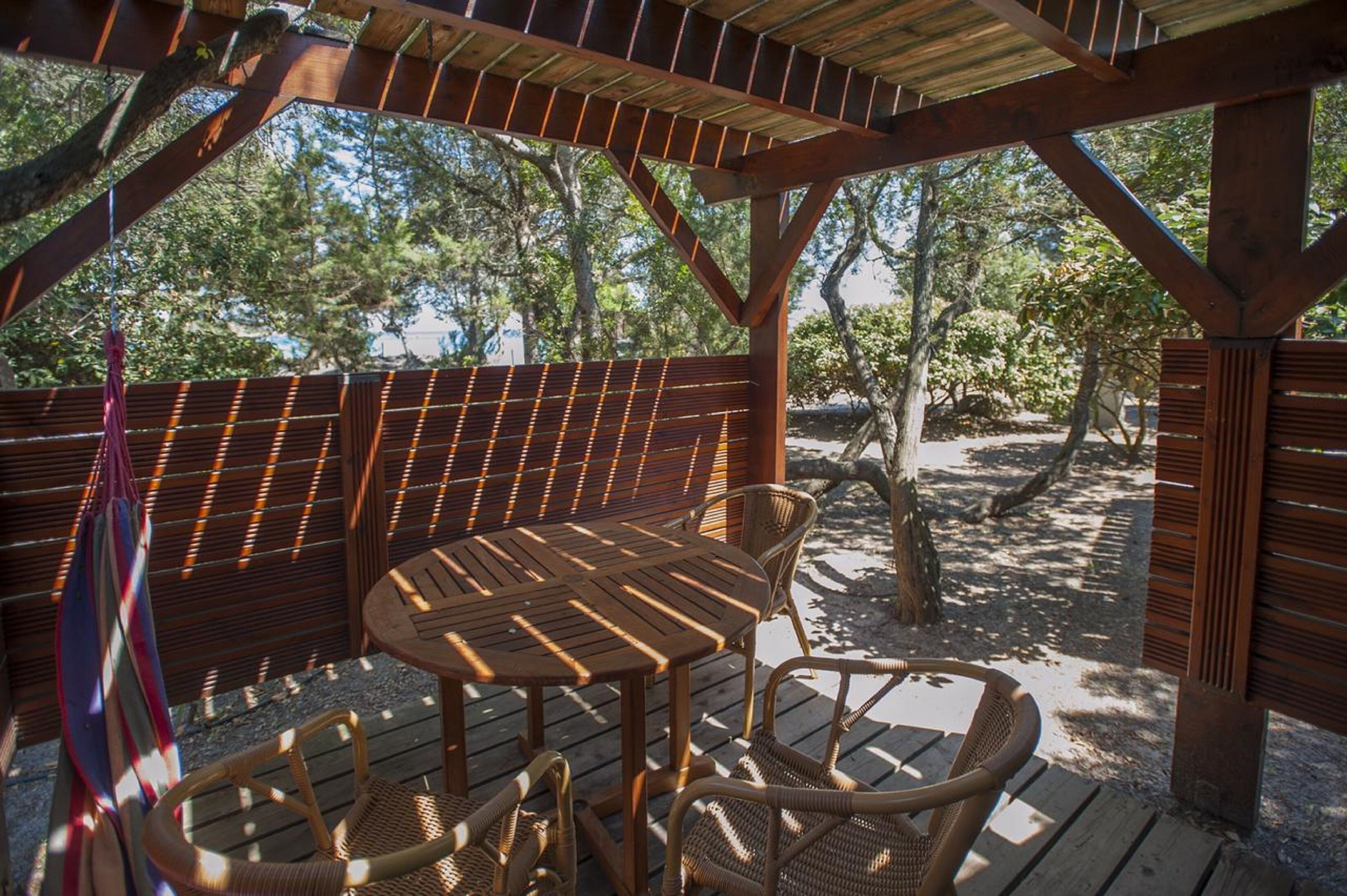An outdoor wooden deck with a table and chairs, surrounded by wooden railings and trees.