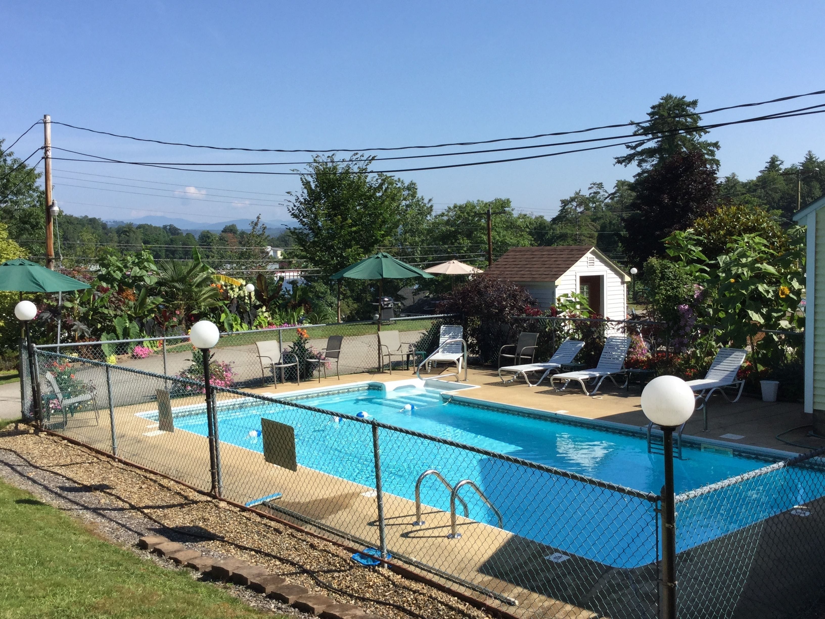 Une piscine dotée d’une terrasse entourée d’une clôture, de chaises longues et de parasols.