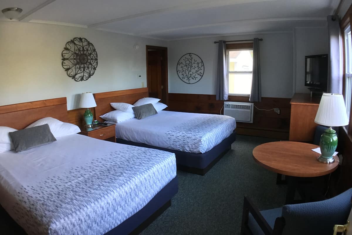 A hotel room with two beds, a desk with a chair, a television, and decorative wall art.