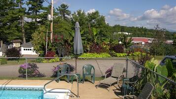 A pool area with a diving board, lounge chairs, and a covered umbrella.