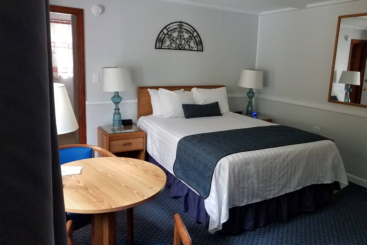A hotel room with a bed, two bedside tables with lamps, a round wooden table, and a chair.