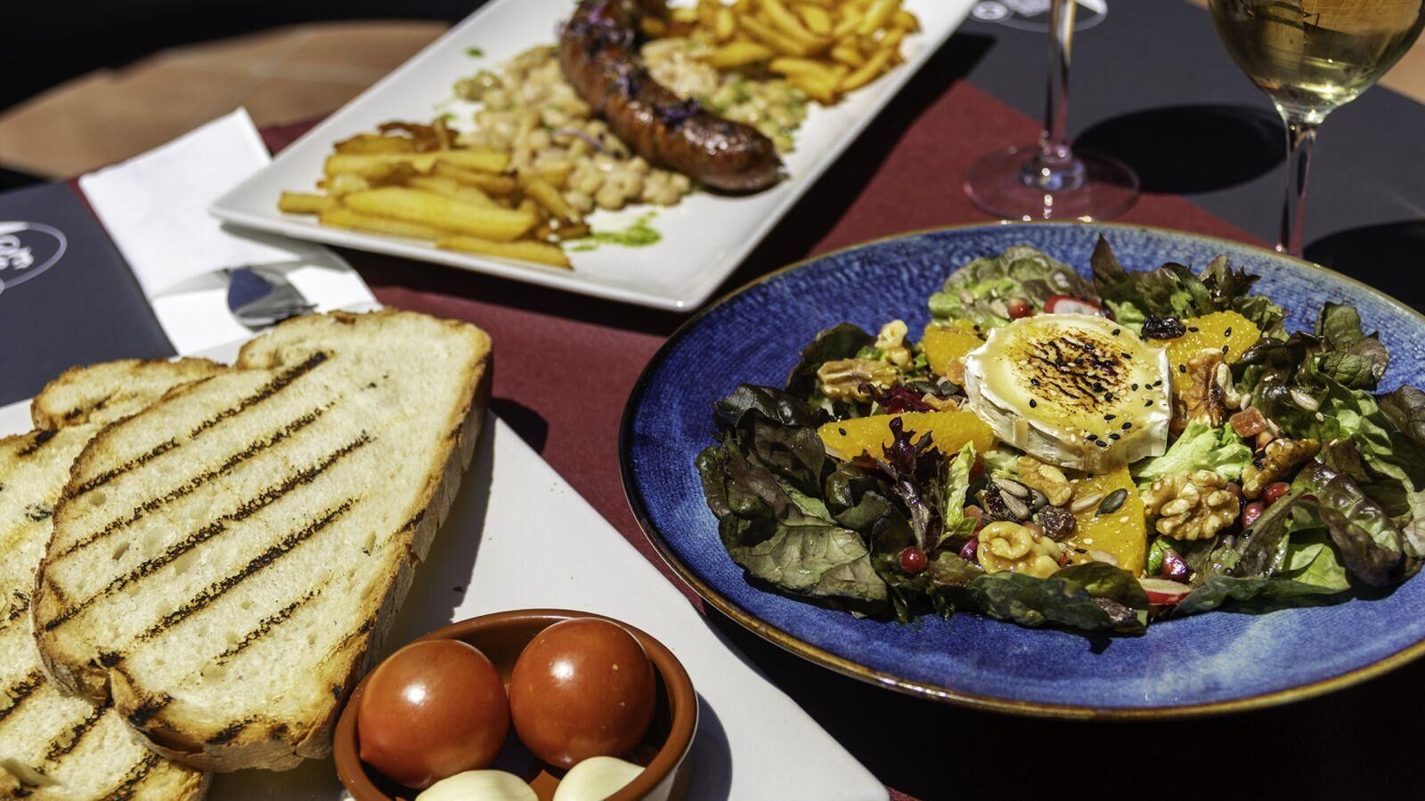 Un repas composé de pain grillé, d’une salade aux noix et aux graines, et d’une assiette de frites et de viande.