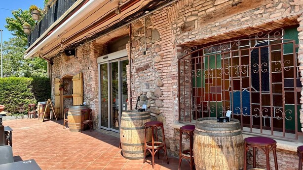 Un patio al aire libre con muros de piedra, barriles de madera y rejas de metal en las ventanas.