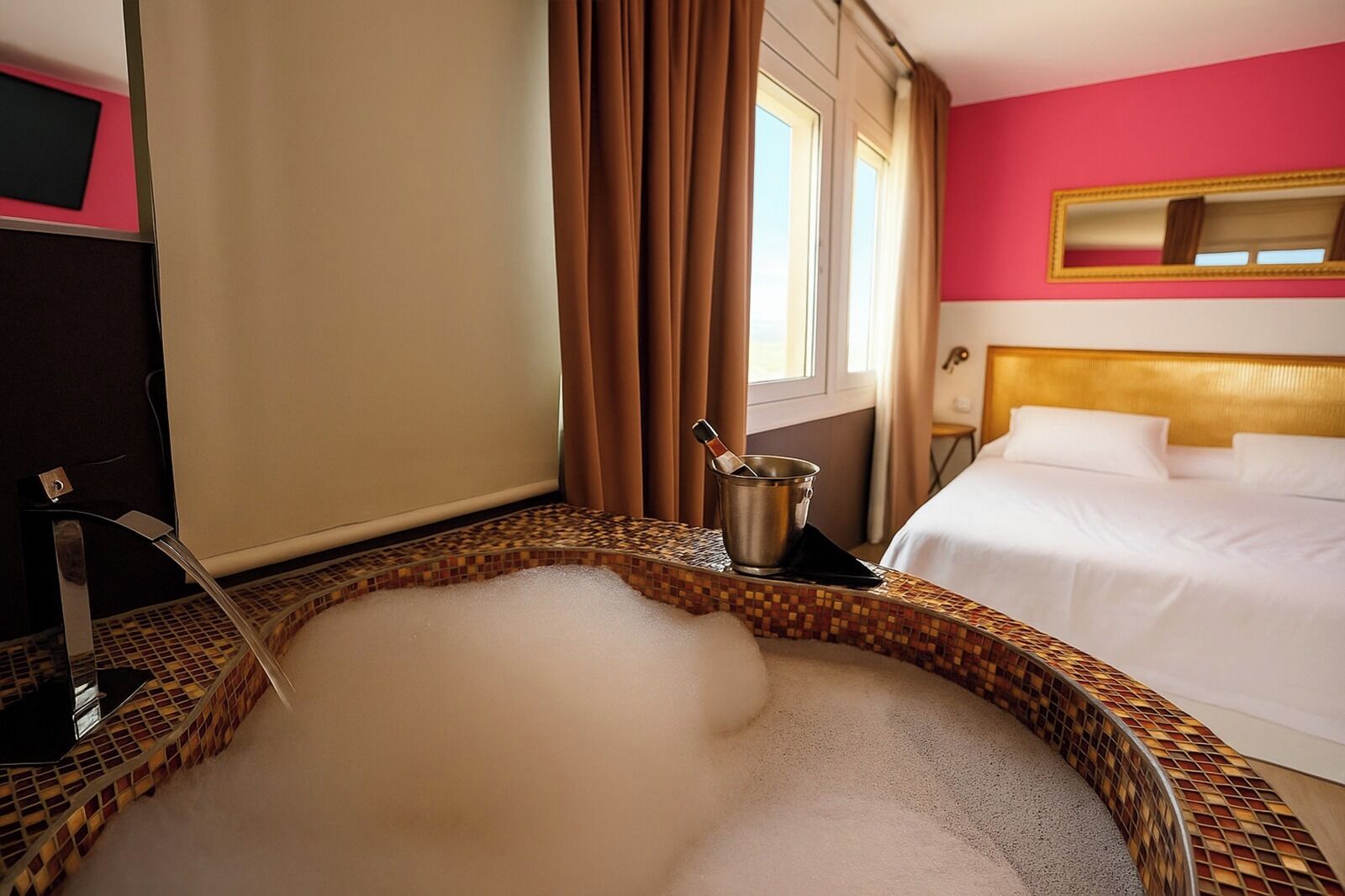 Una habitación de hotel con una bañera grande, una cama y un espejo en la pared.