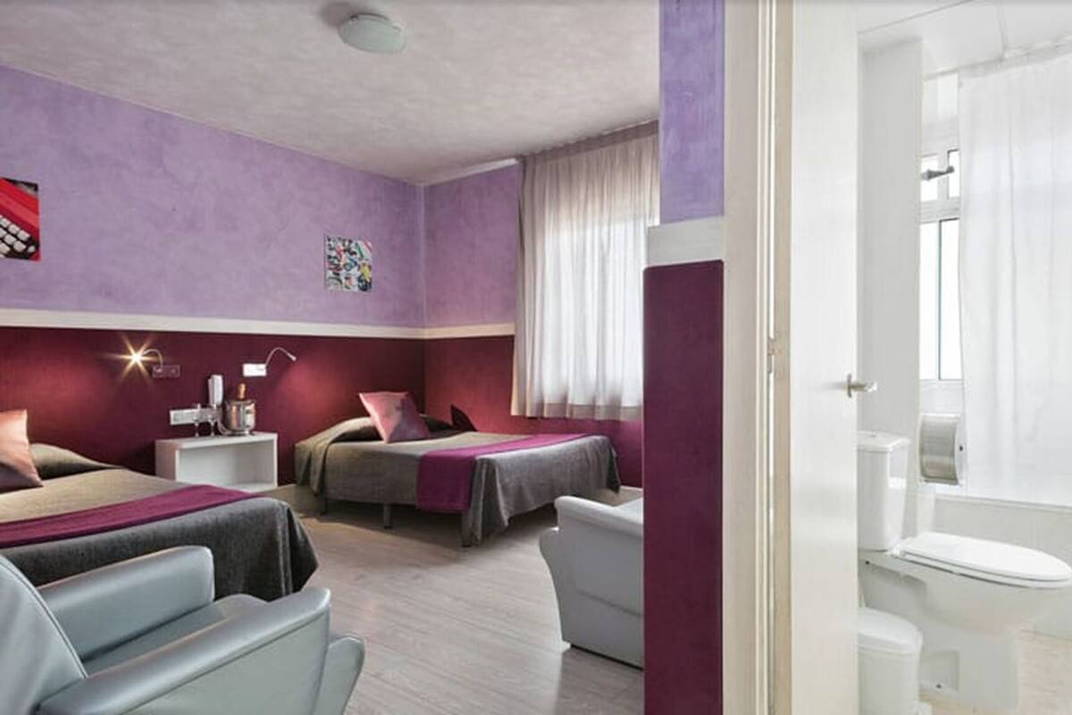 Habitación de hotel con dos camas, un escritorio, una silla, un baño y una ventana con cortinas.